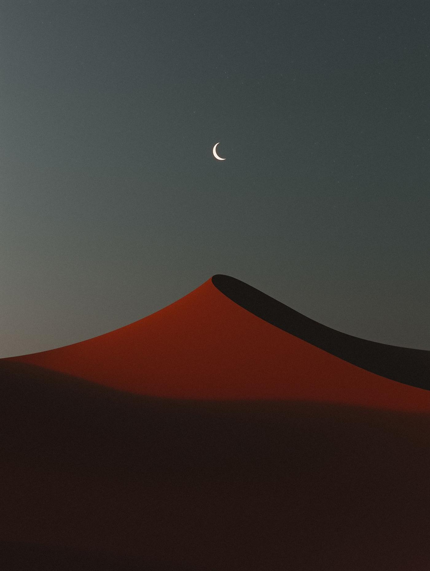A red dune at dusk under a crescent moon